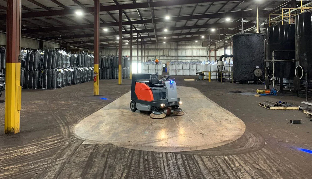 Technician deep cleaning factory floor using heavy-duty scrubbing machine